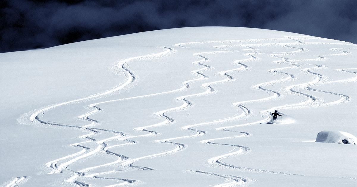 A lone skier’s winding tracks through fresh powder on a snowy slope.