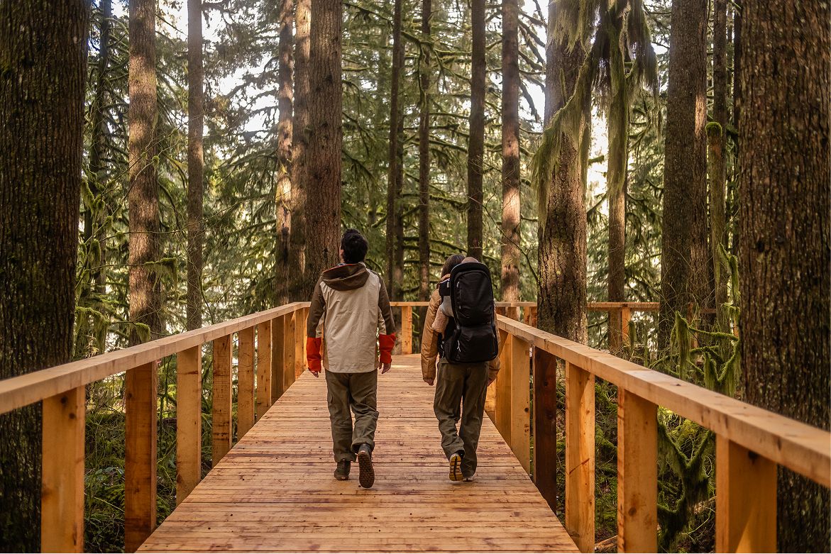 Two hikers walking a wooden walkway through the forest