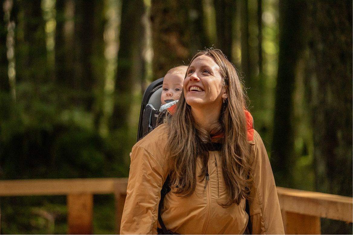 A woman with a baby on her back smiling in the forest