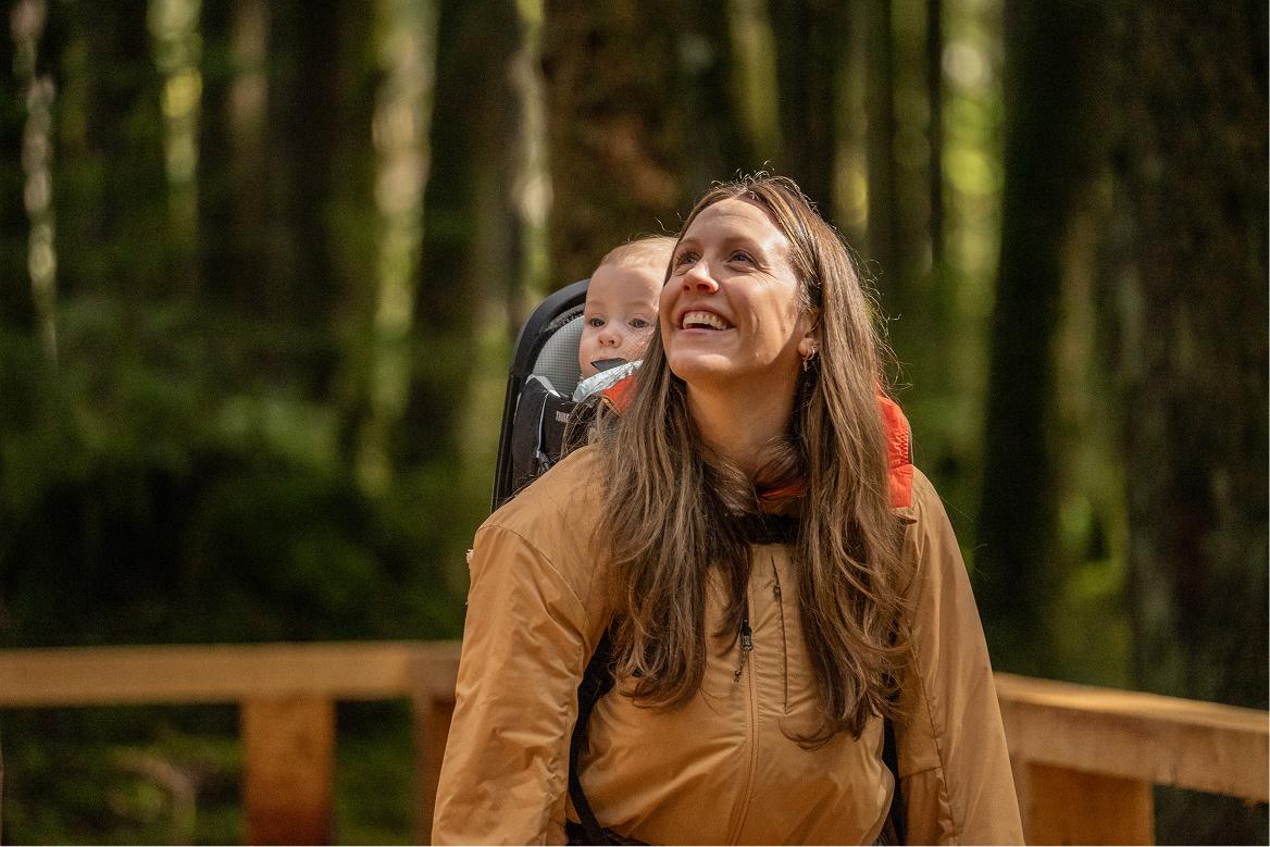 A woman with a baby on her back smiling in the forest