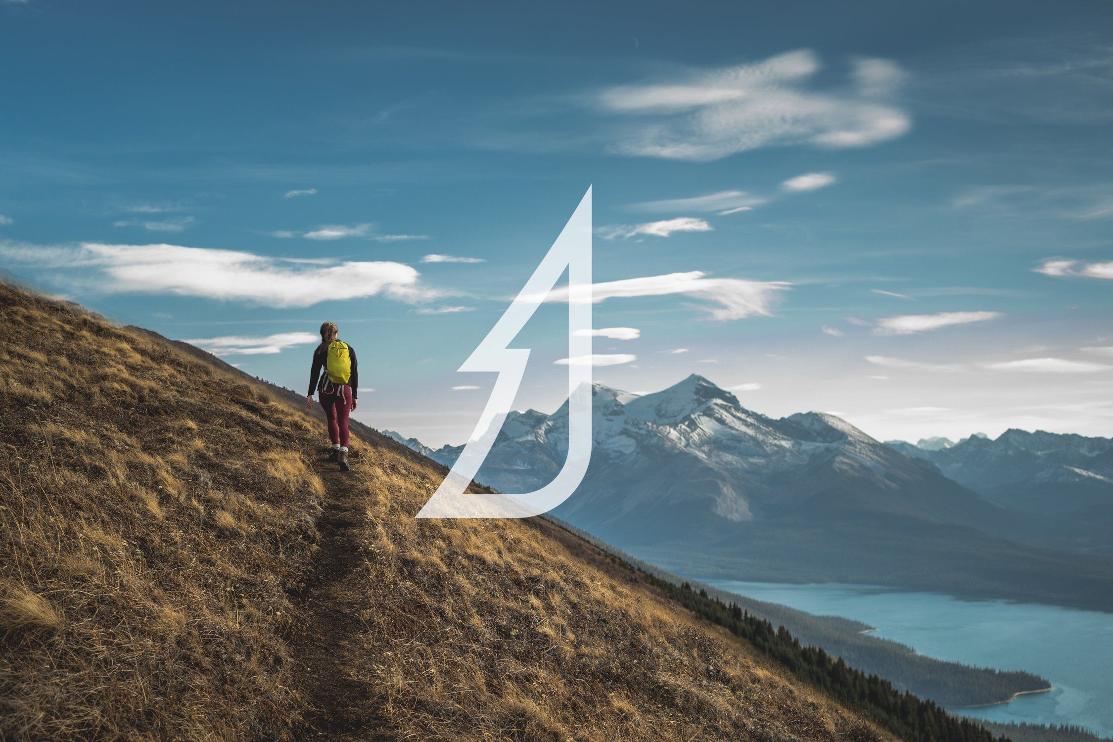 A hiker on a ridge above a lake, with the Tourism Jasper mark