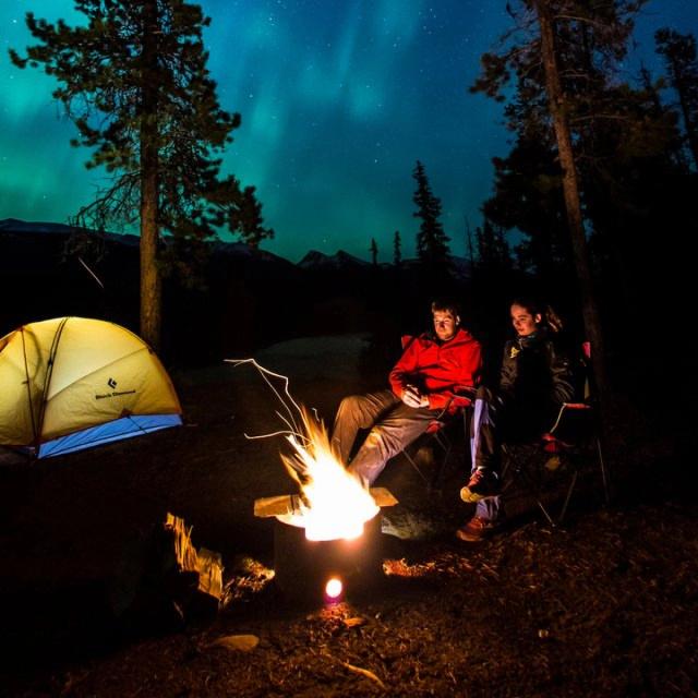 Campers around a fire under the northern lights