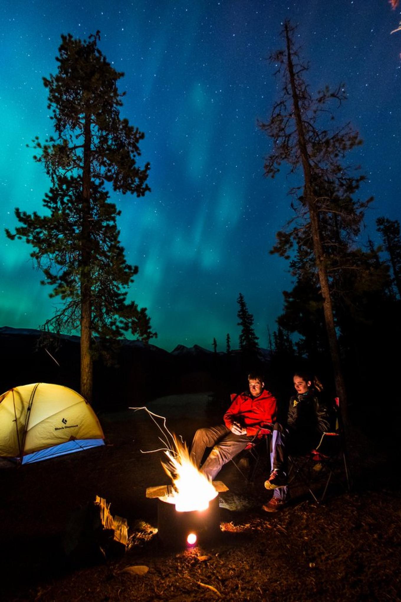 Campers around a fire under the northern lights