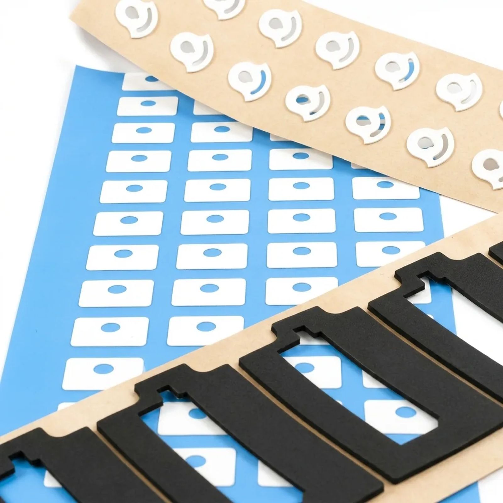 Portrait view of rotary die-cut grommets, white pads on blue liner and black foam gaskets from Cannon Gasket.