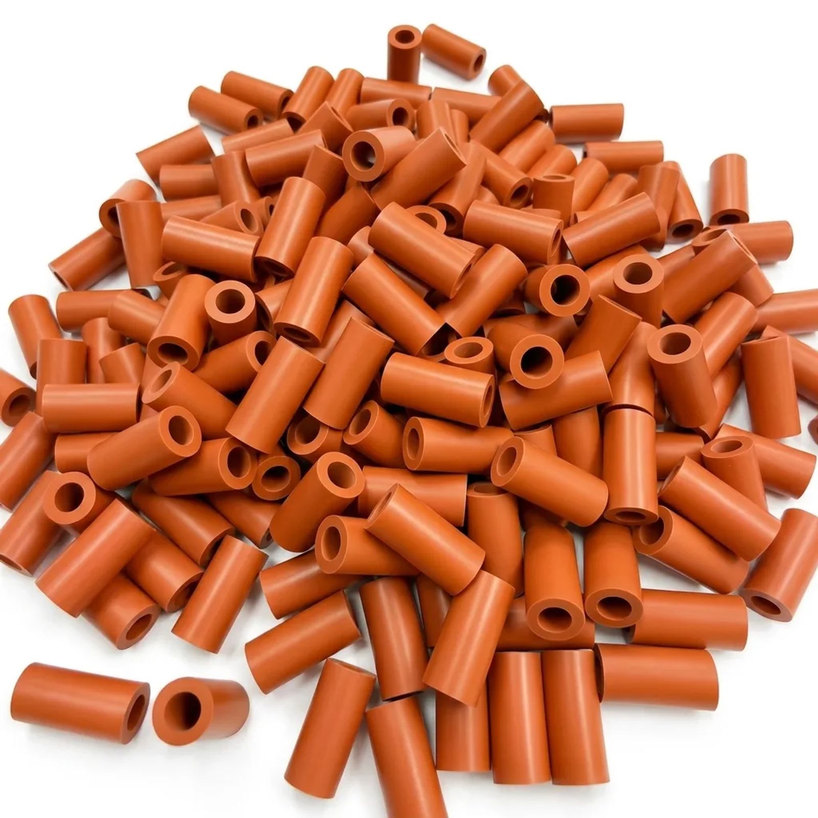 Pile of orange silicone rubber tubular spacers with center bores on a clean white background.