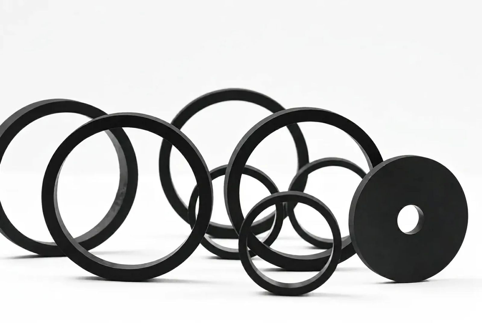 Assorted lathe-cut black rubber rings, seals, and a solid washer arranged on a white background.