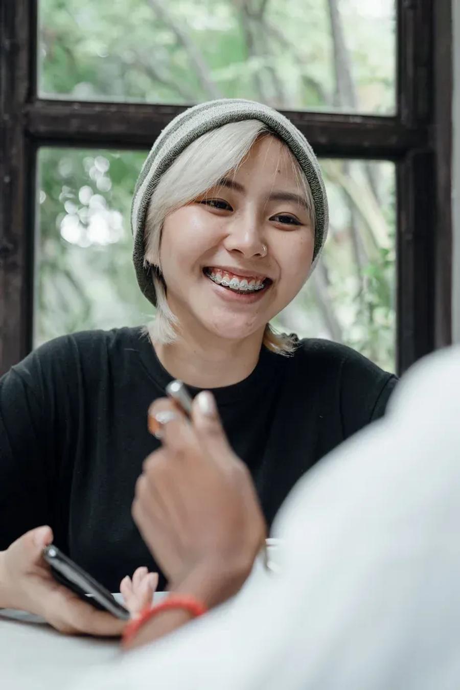 A smiling patient with braces chatting across a table