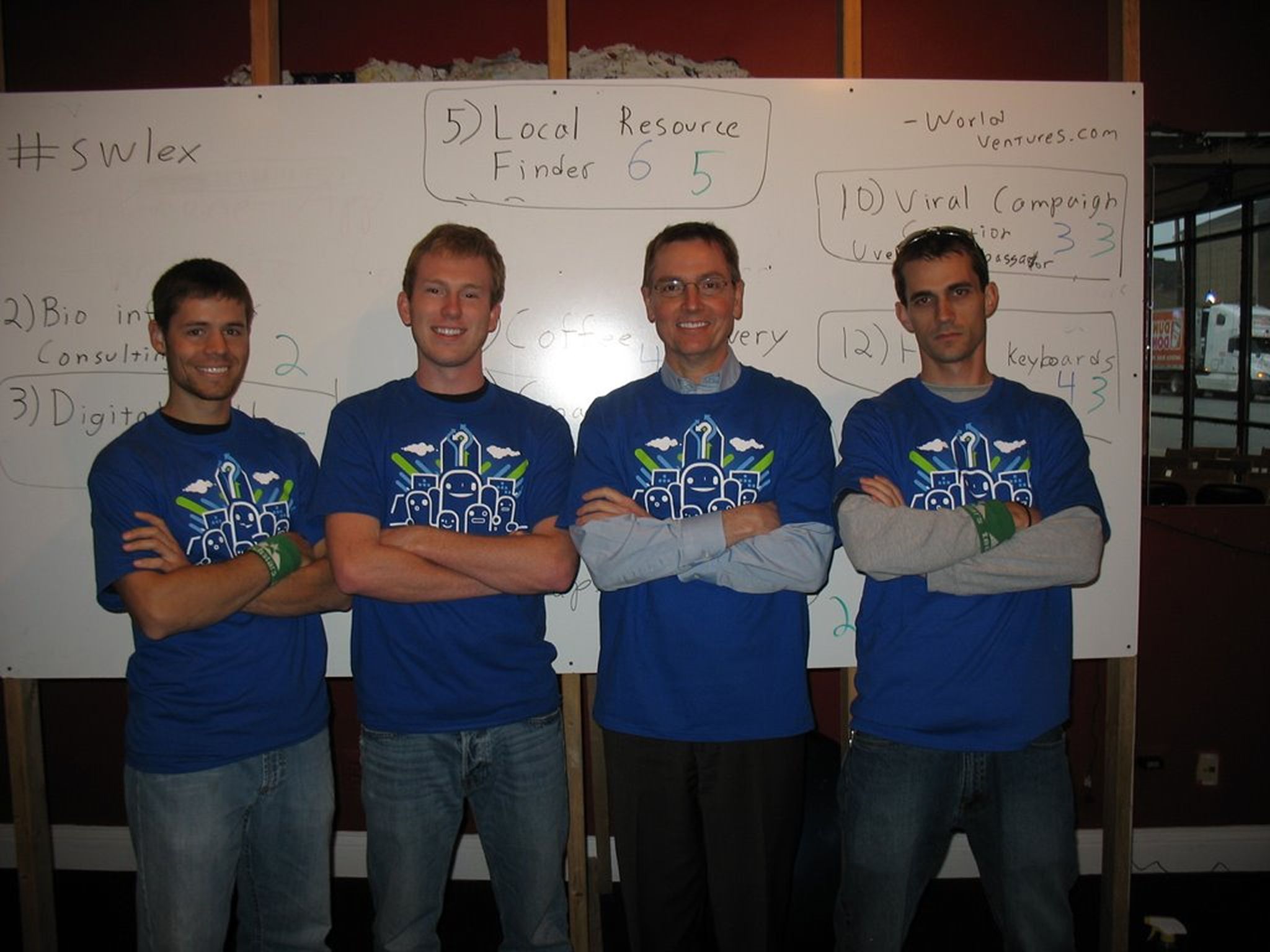 Four founders with blue awesome inc tees in front of a wipeboard
