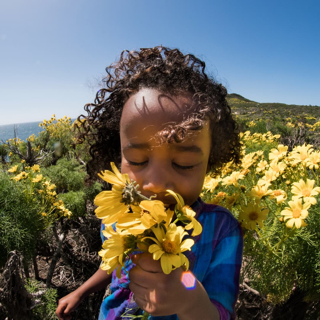 A young Black girls sniffs the bundle of yellow flowers she has in her hand.
