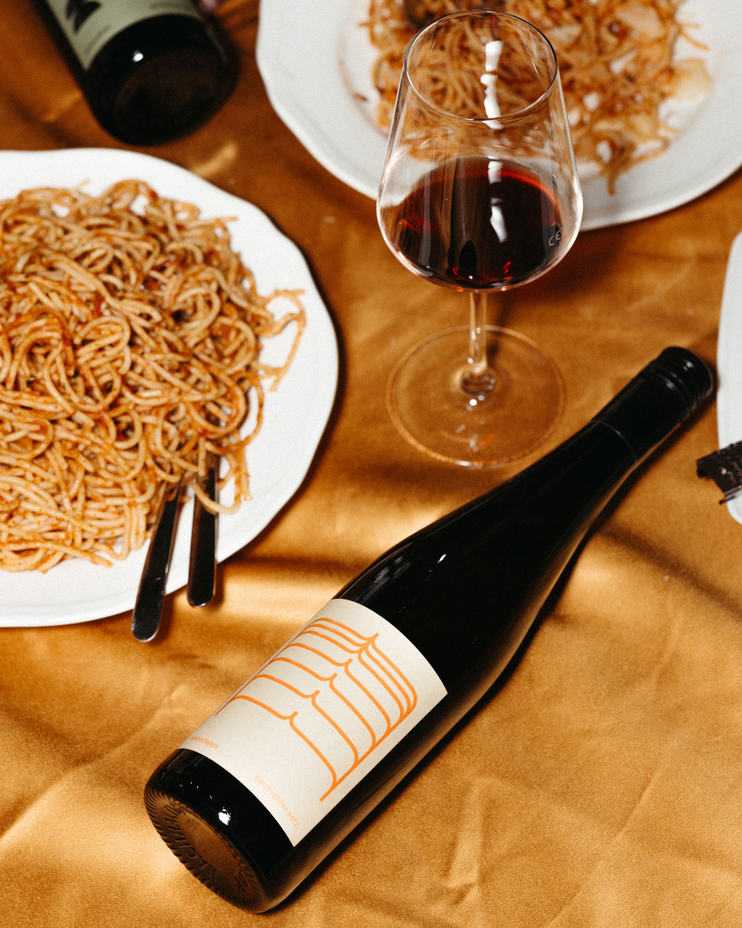 Esstisch-Szene mit Weinflasche und Spaghetti auf orangenem Tischtusch