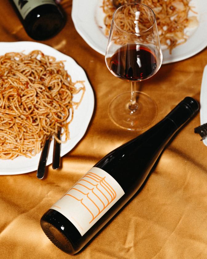 Esstisch-Szene mit Weinflasche und Spaghetti auf orangenem Tischtusch