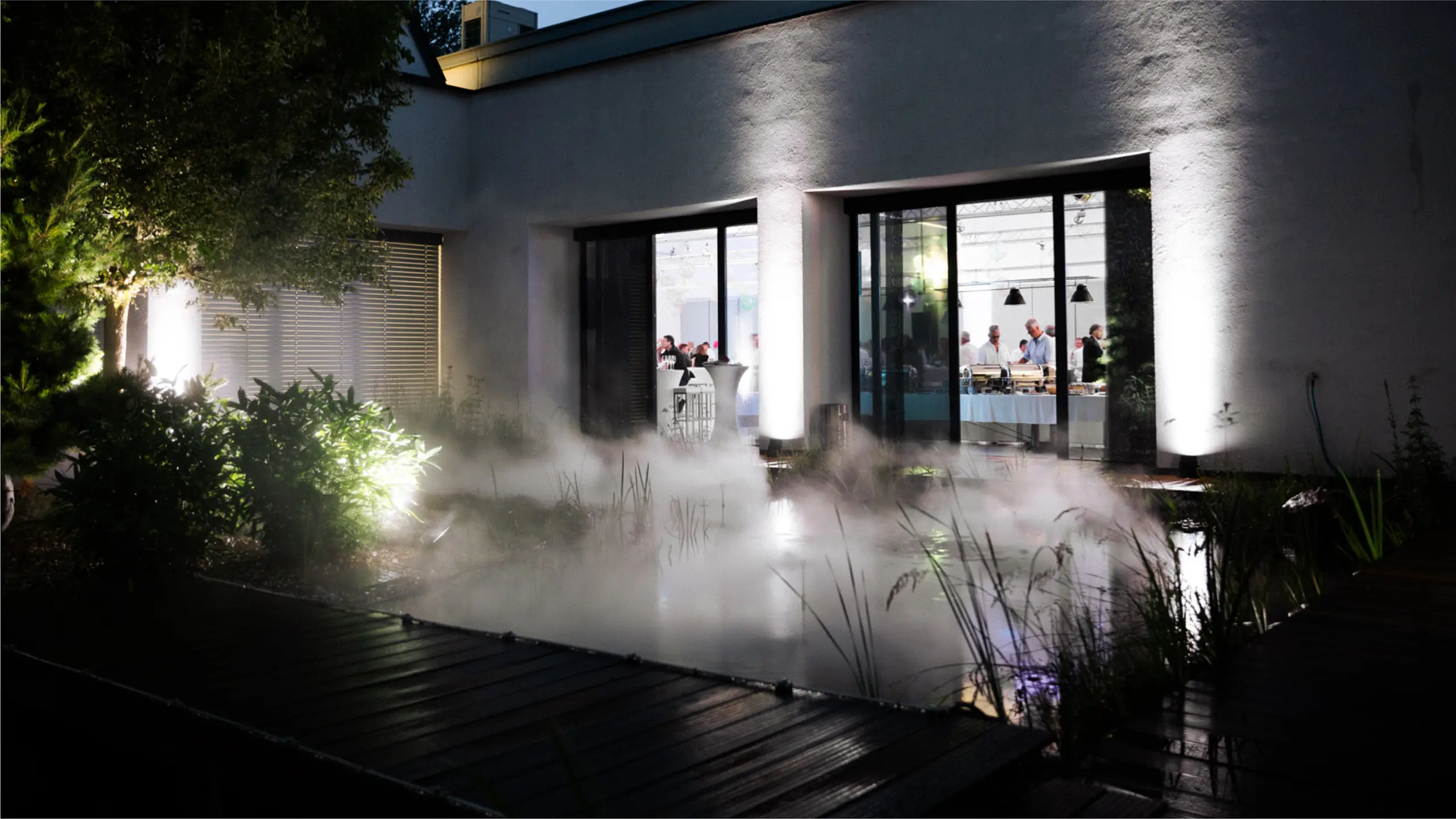 Gartenszene mit Rauch- und Lichtinstallation in Garten vor modernem Haus