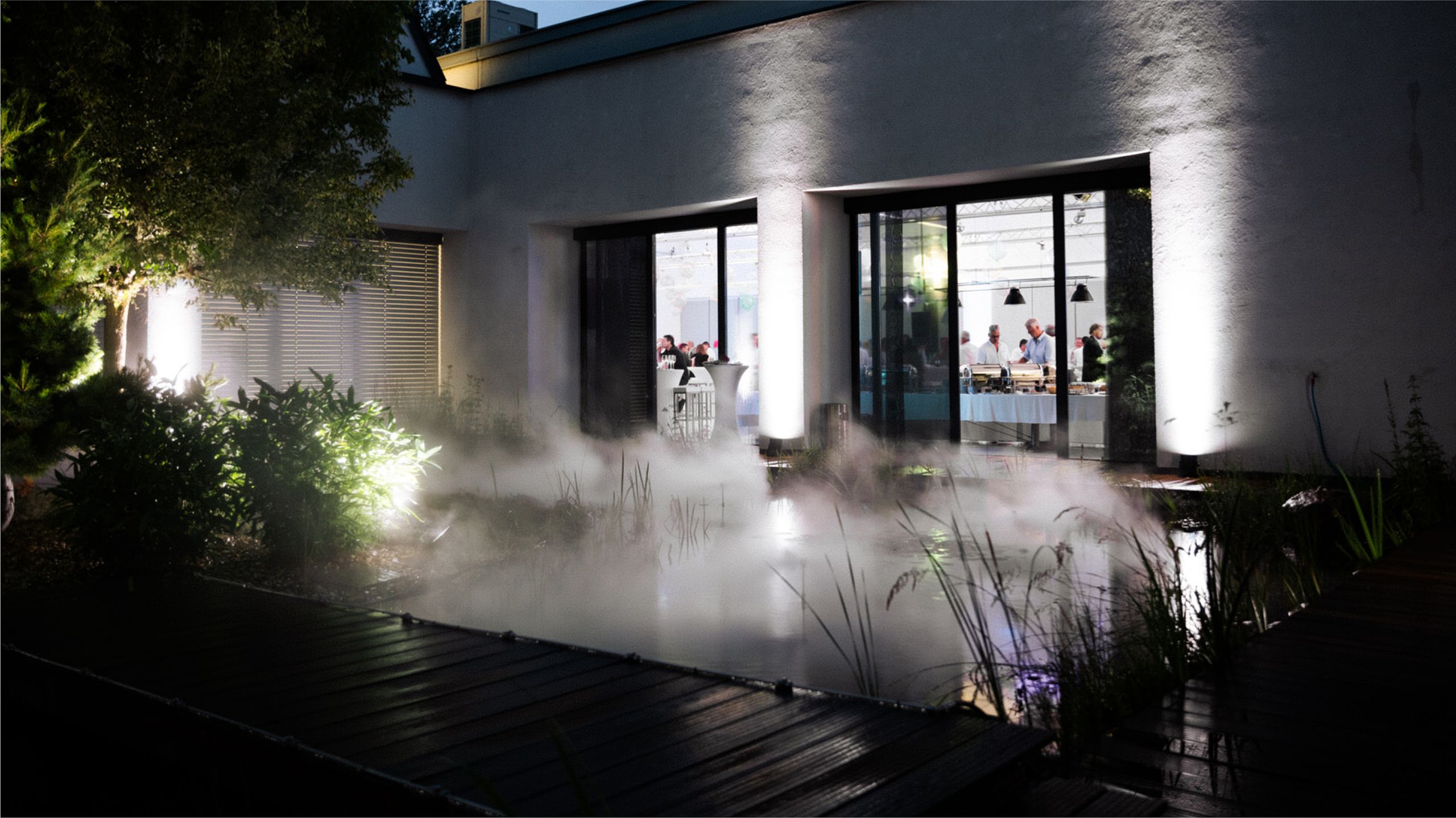 Gartenszene mit Rauch- und Lichtinstallation in Garten vor modernem Haus
