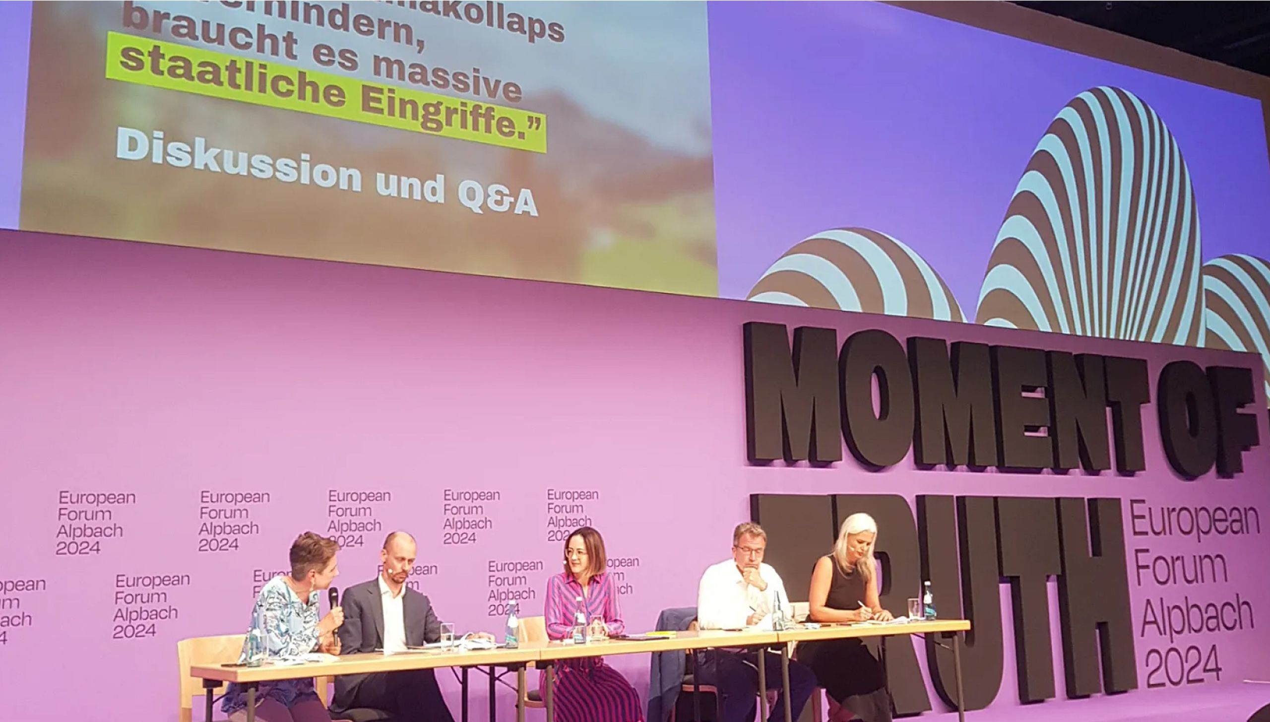 Podiumsdiskussion mit mehreren Sprecher:innen auf Bühne