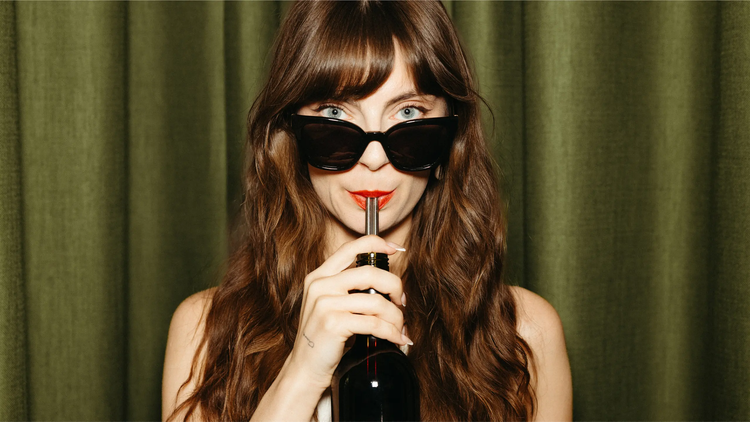 Model drinking wine directly from the bottle with a straw