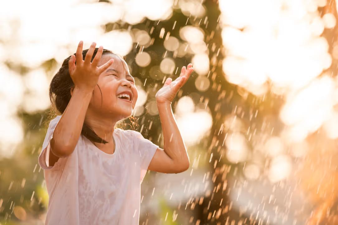Girl laughing under a water sprinkler