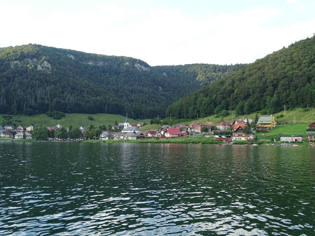 A Slovak village on the shore of a lake below forested hills.