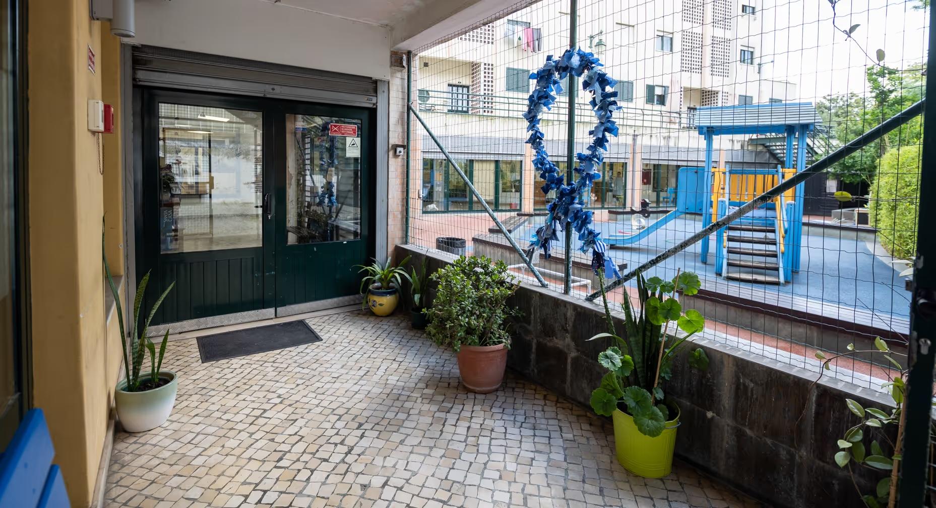 Entrance area with potted plants, tiled floor, and a netted railing overlooking a blue playground slide.