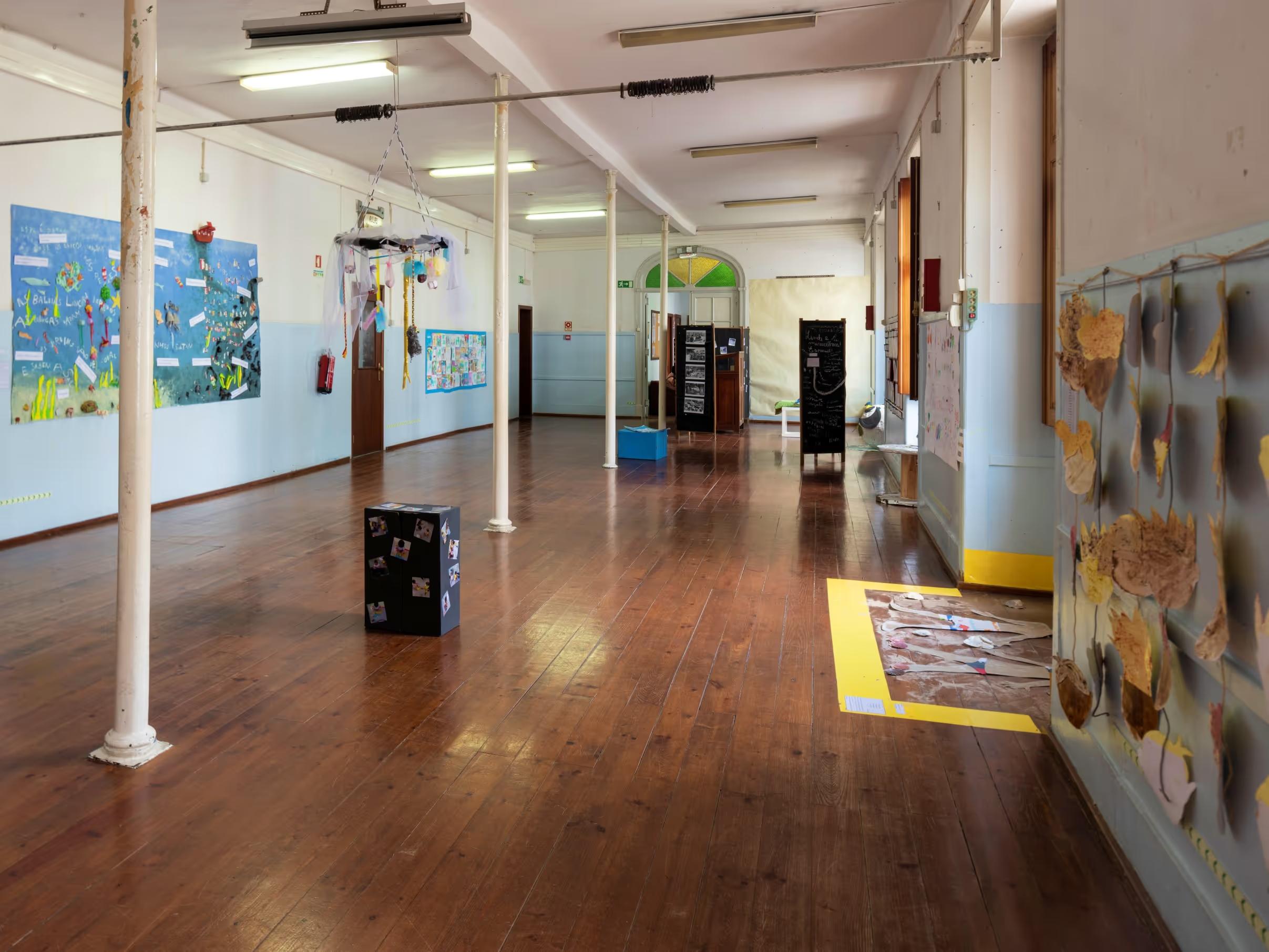 Empty room with wooden floor, white pillars, children's artwork on walls, and hanging craft decorations.