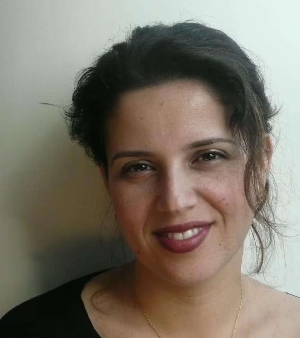Smiling woman with dark hair pulled back, wearing a black top and light makeup, against a plain light background.