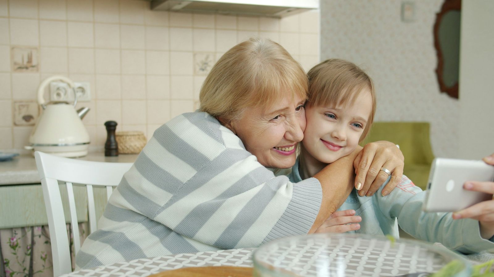 A grandmother and her granddaughter laugh together at the kitchen table.