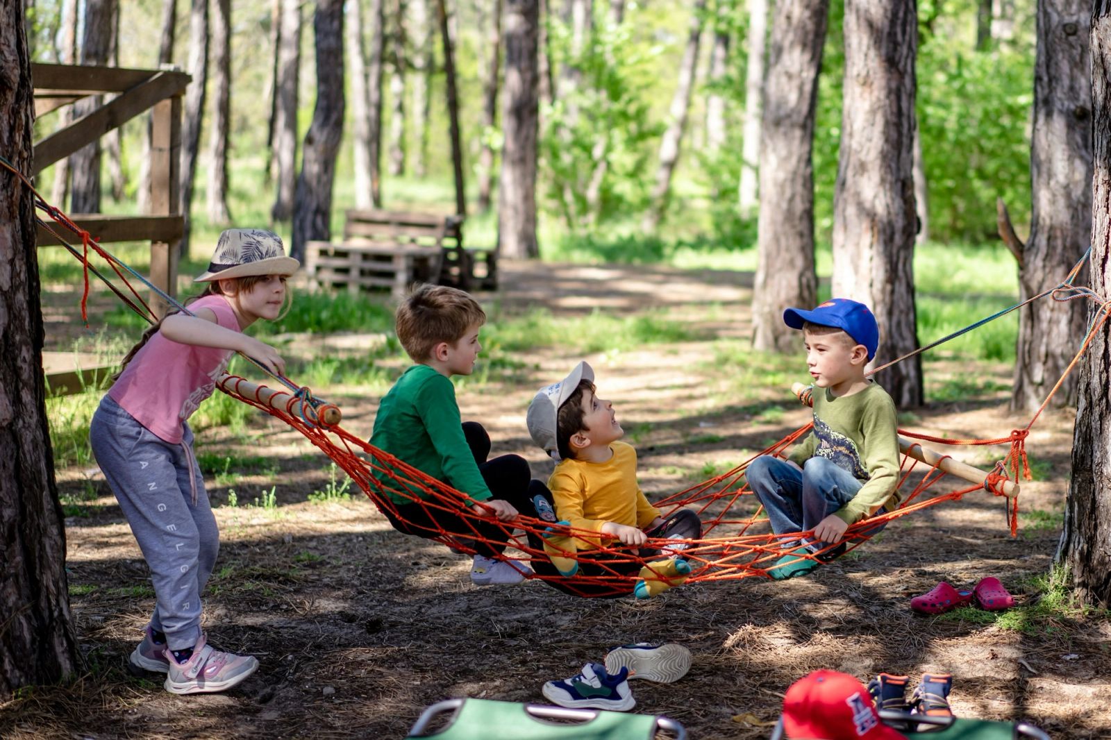 Young children play together around a hammock in a woodland playground.