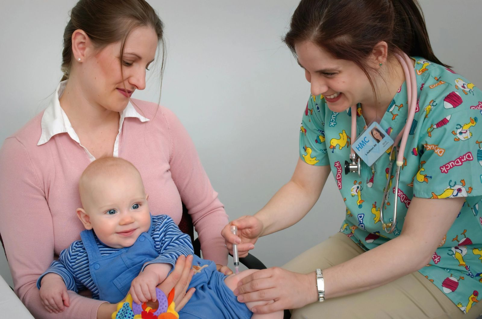 A nurse examines a smiling baby held on its mother’s lap.