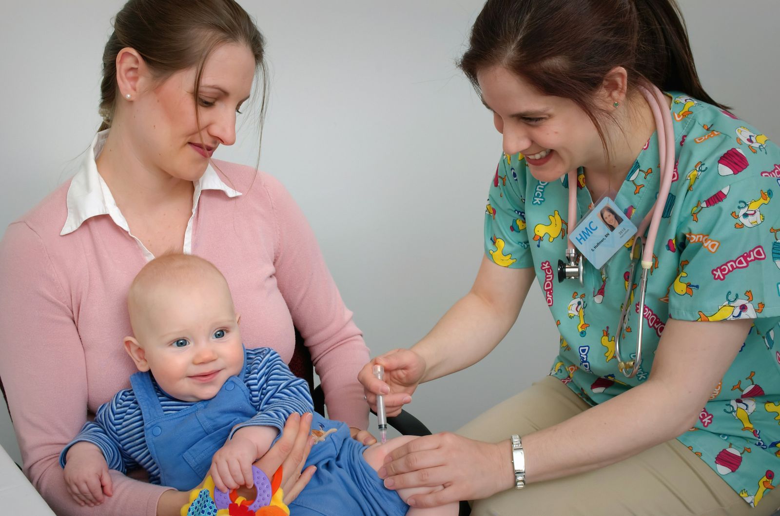 A nurse examines a smiling baby held on its mother’s lap.