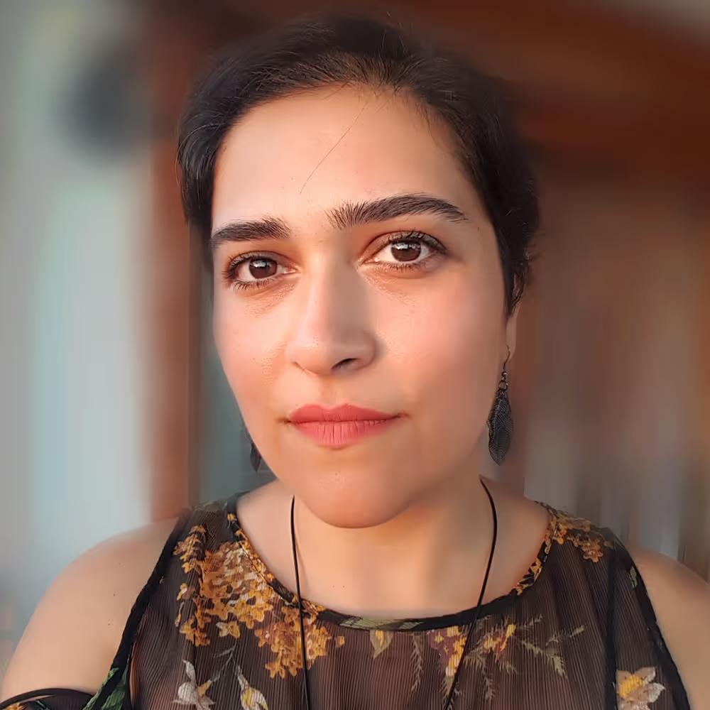 Close-up portrait of a woman with dark hair, wearing a floral-patterned top and leaf-shaped earrings, looking directly at the camera.