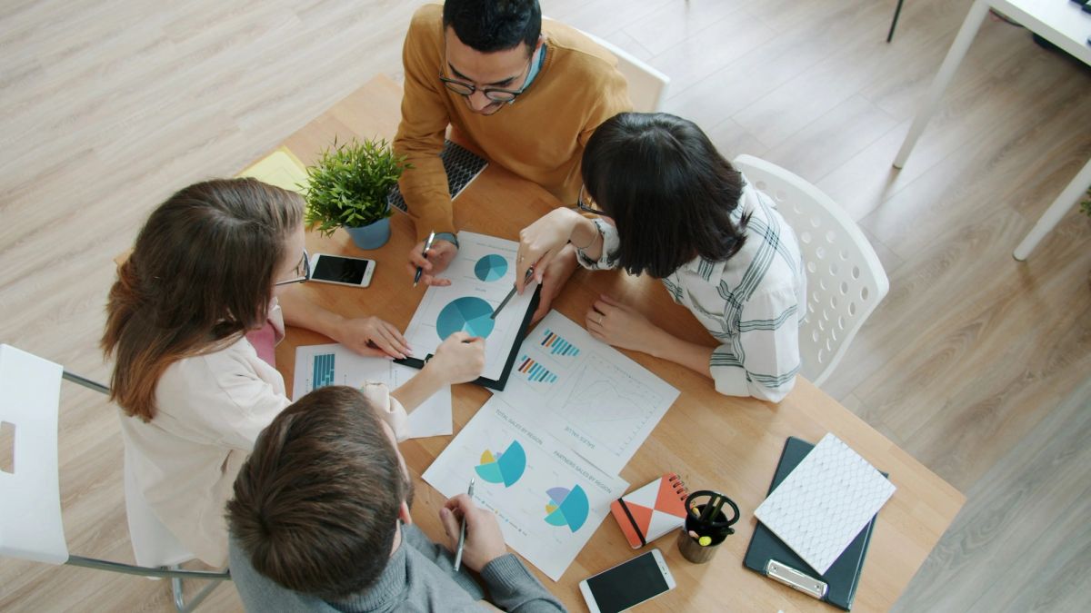 Colleagues work together around a table covered in charts and notes.
