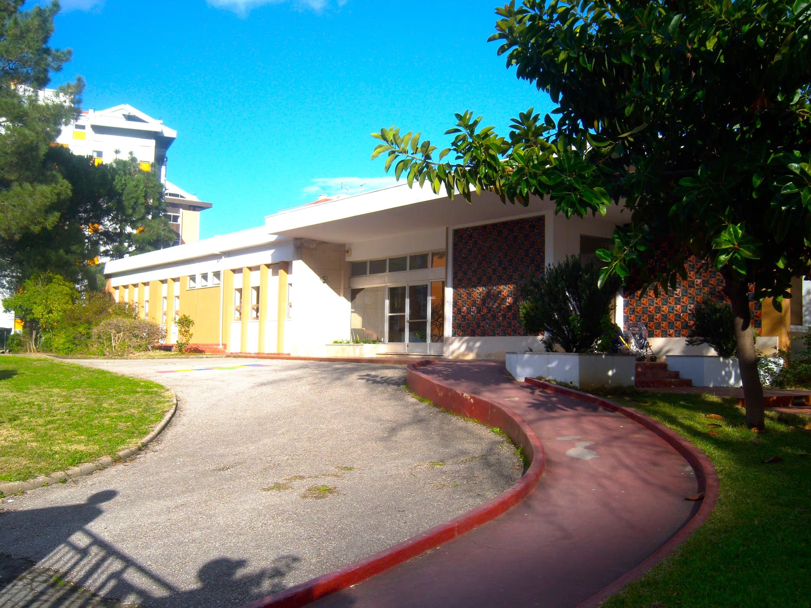 Single-story building with a curved red pathway, trees, and clear blue sky on a sunny day.
