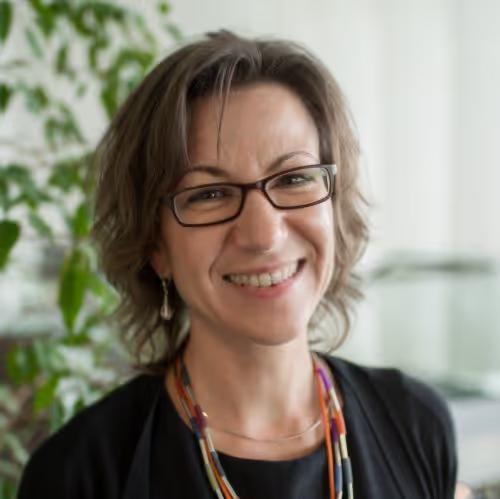 Smiling woman with short brown hair and glasses wearing colorful beaded necklaces and a black top.