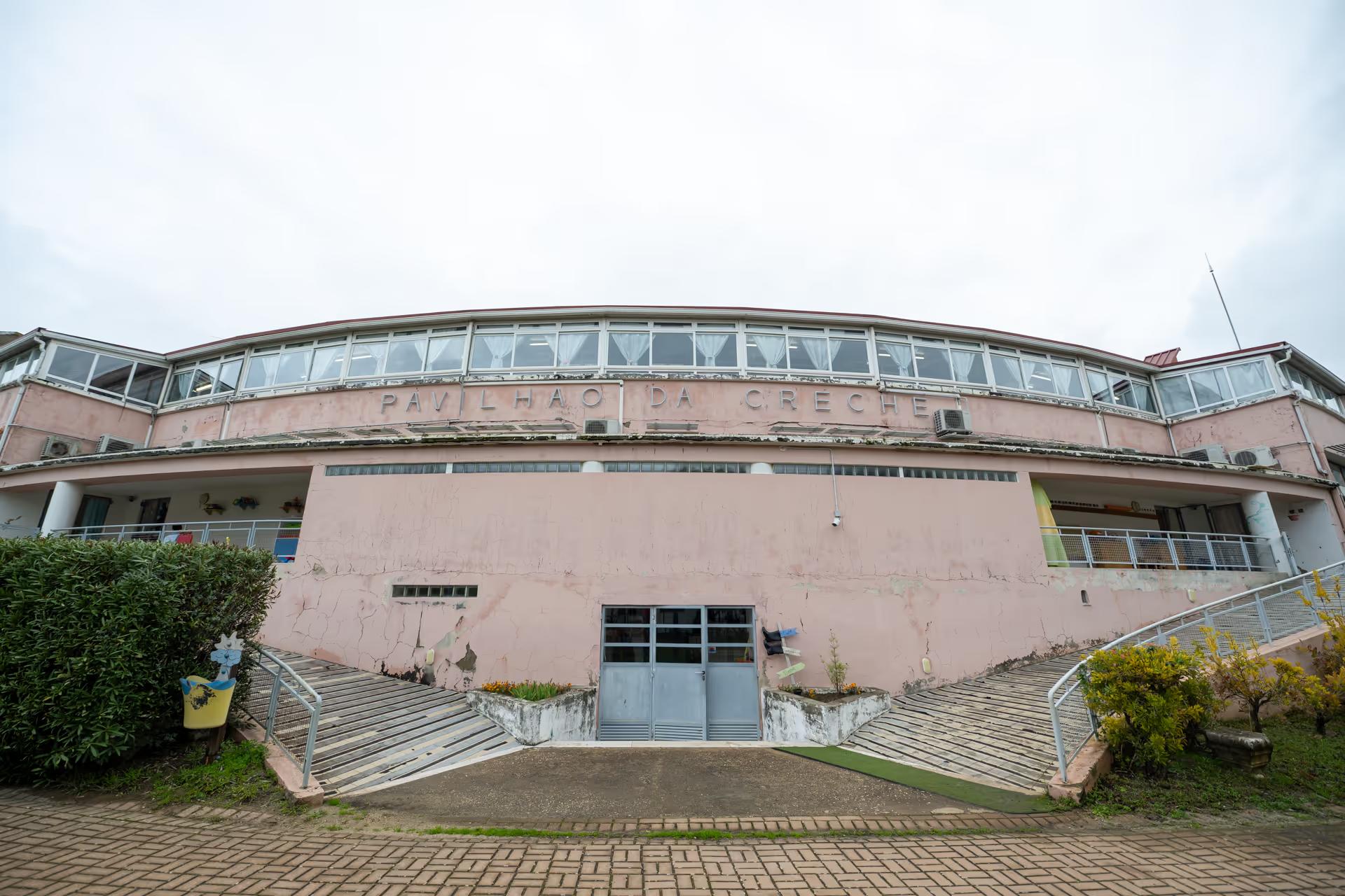 Curved pink building with ramps on each side and sign reading Pavilhão da Creche.