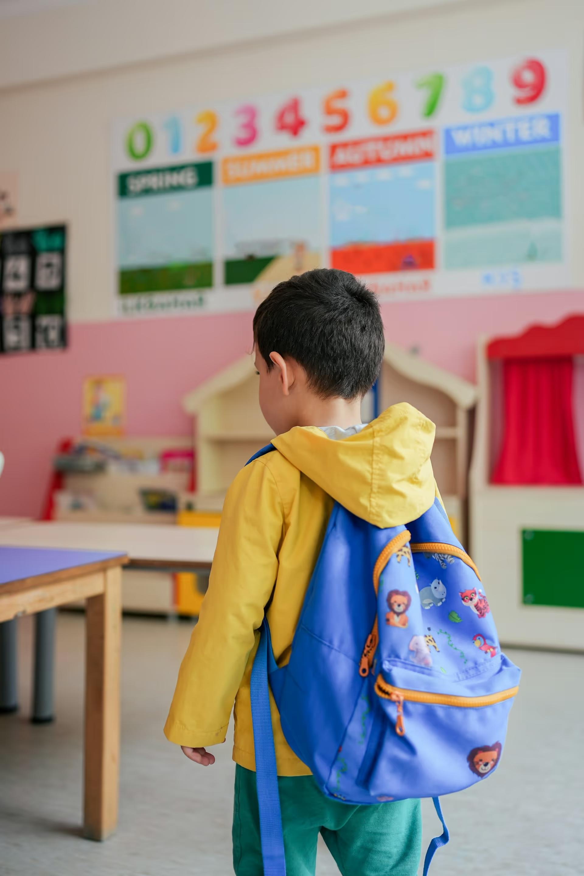 Young child with a backpack standing in a kindergarten classroom