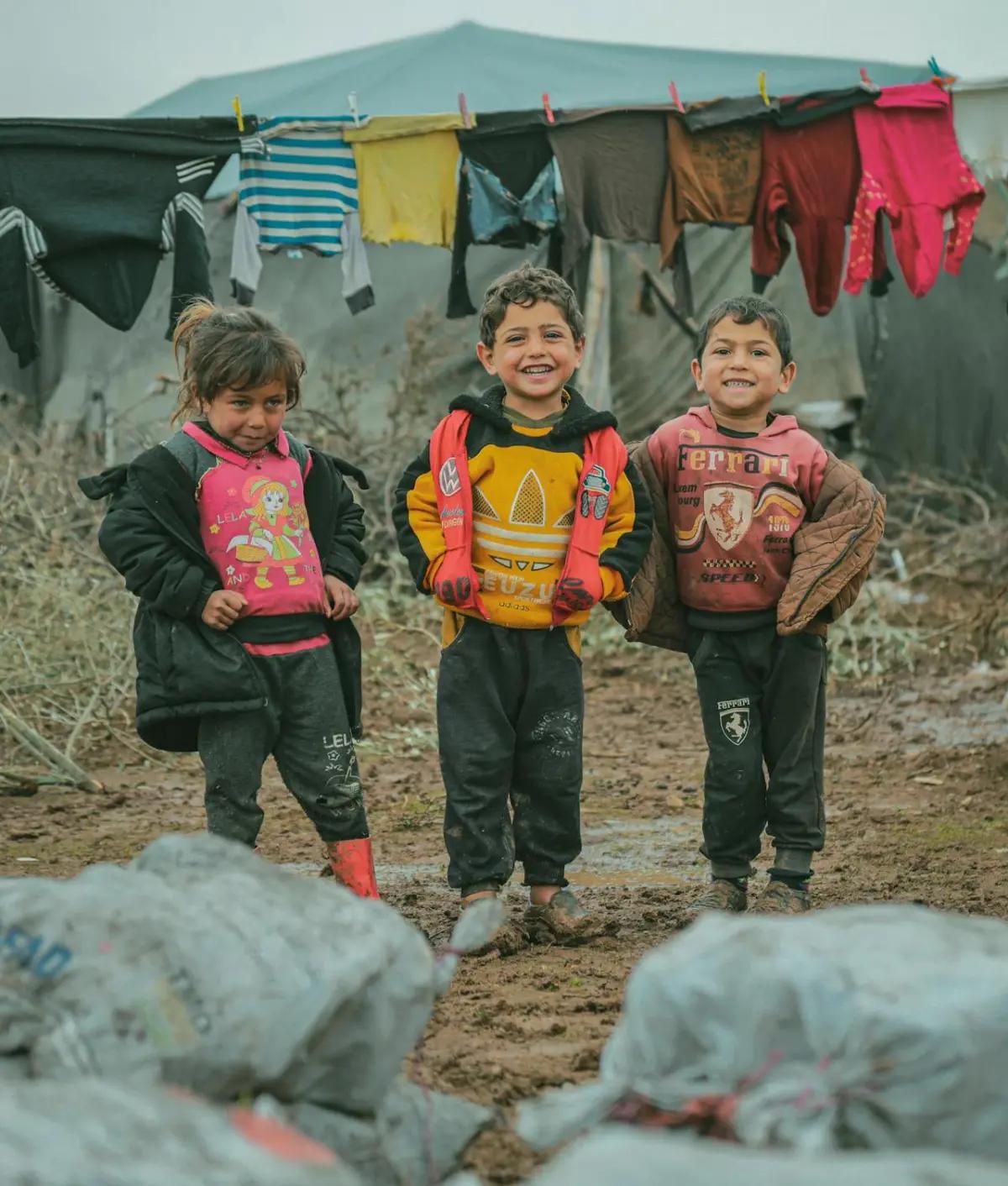 Three children standing in a refugee camp