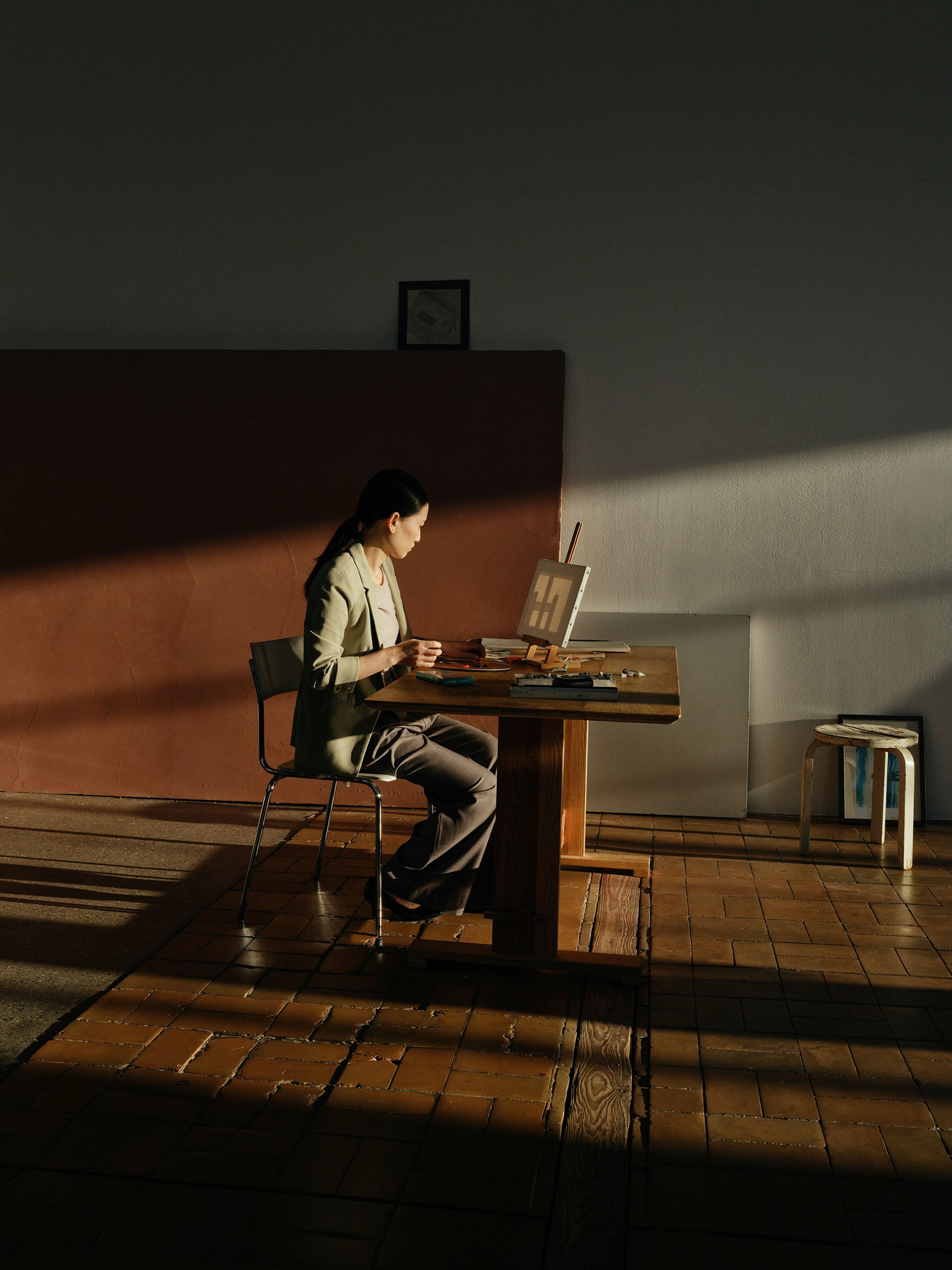 A woman sitting at a desk in a room where the sun is shining in through the windows