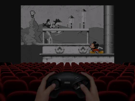 Un giocatore impugna un controller Sega davanti a uno schermo cinematografico con Mickey Mania