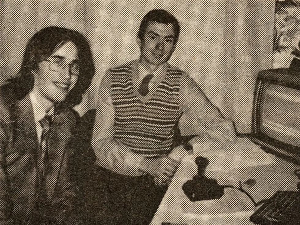 Fotografia storica in bianco e nero di due giovani sviluppatori accanto a un computer, con joystick e televisore.