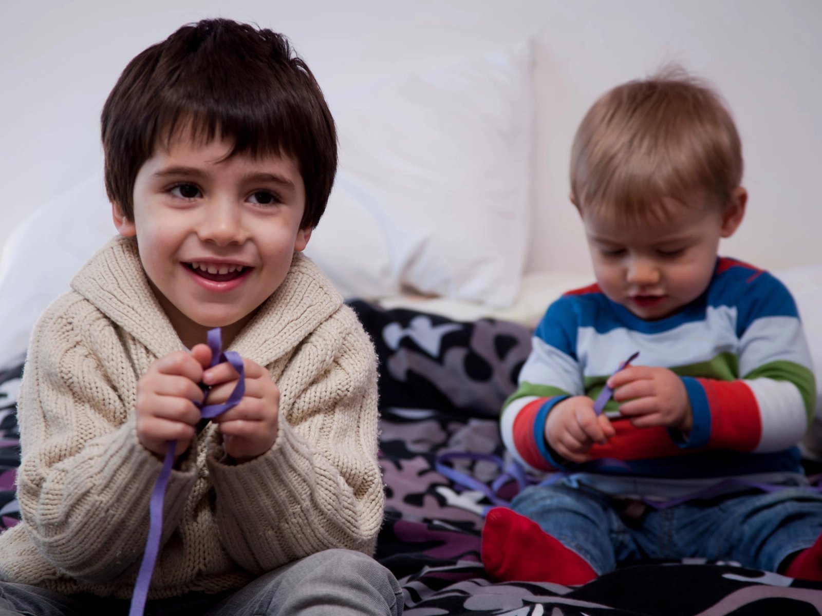 Dos hermanos pequeños jugando sentados en una cama