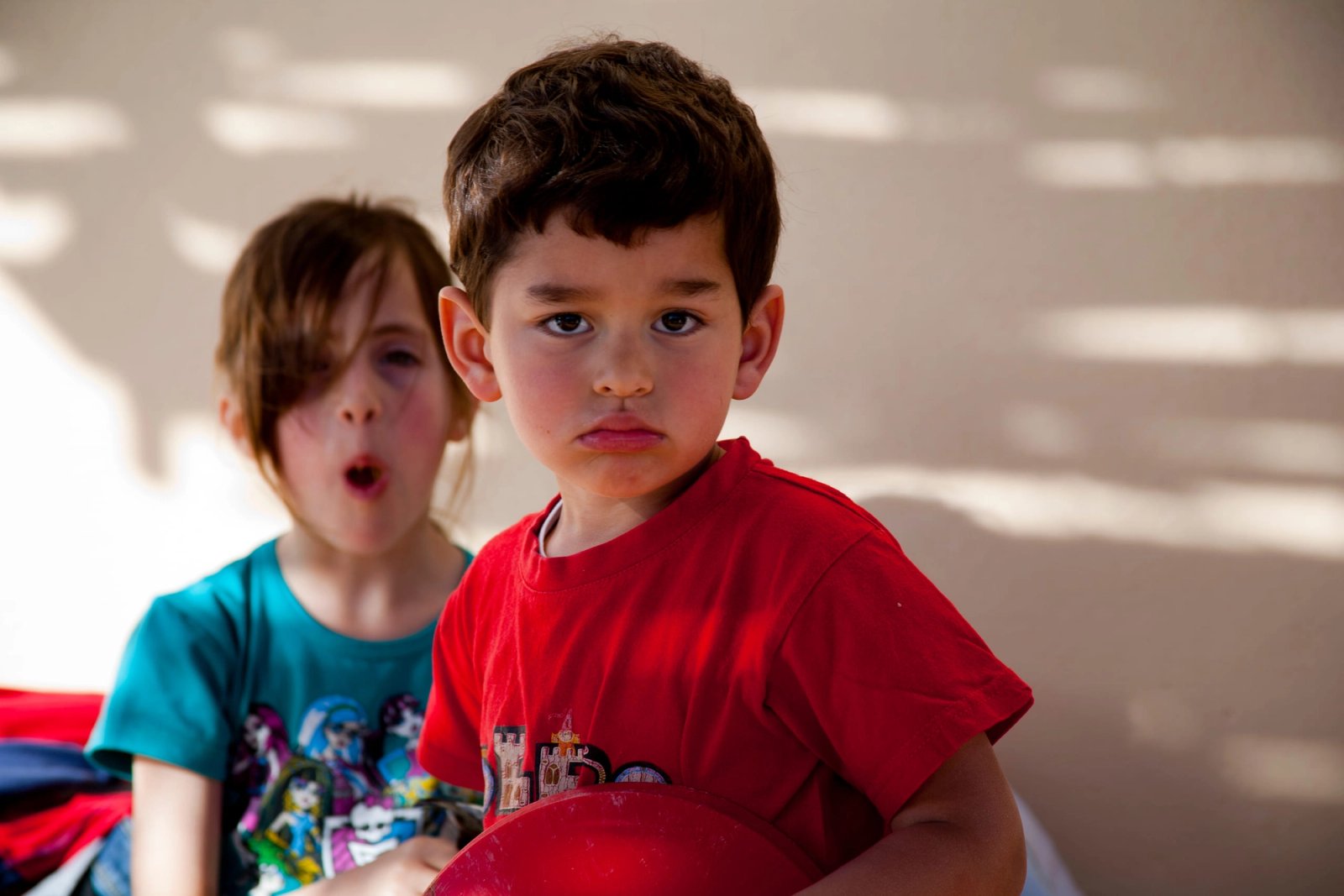 Dos niños pequeños sentados, con la luz rayada de la persiana encima