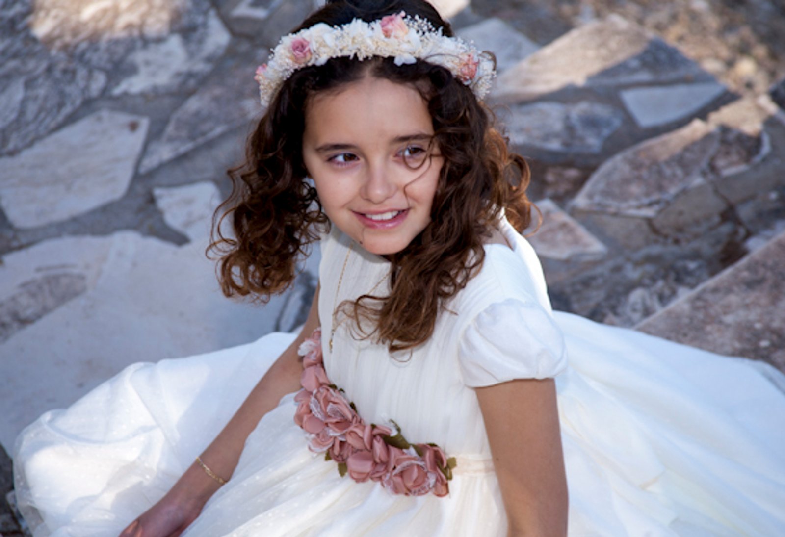 Una niña de comunión sentada sobre las rocas