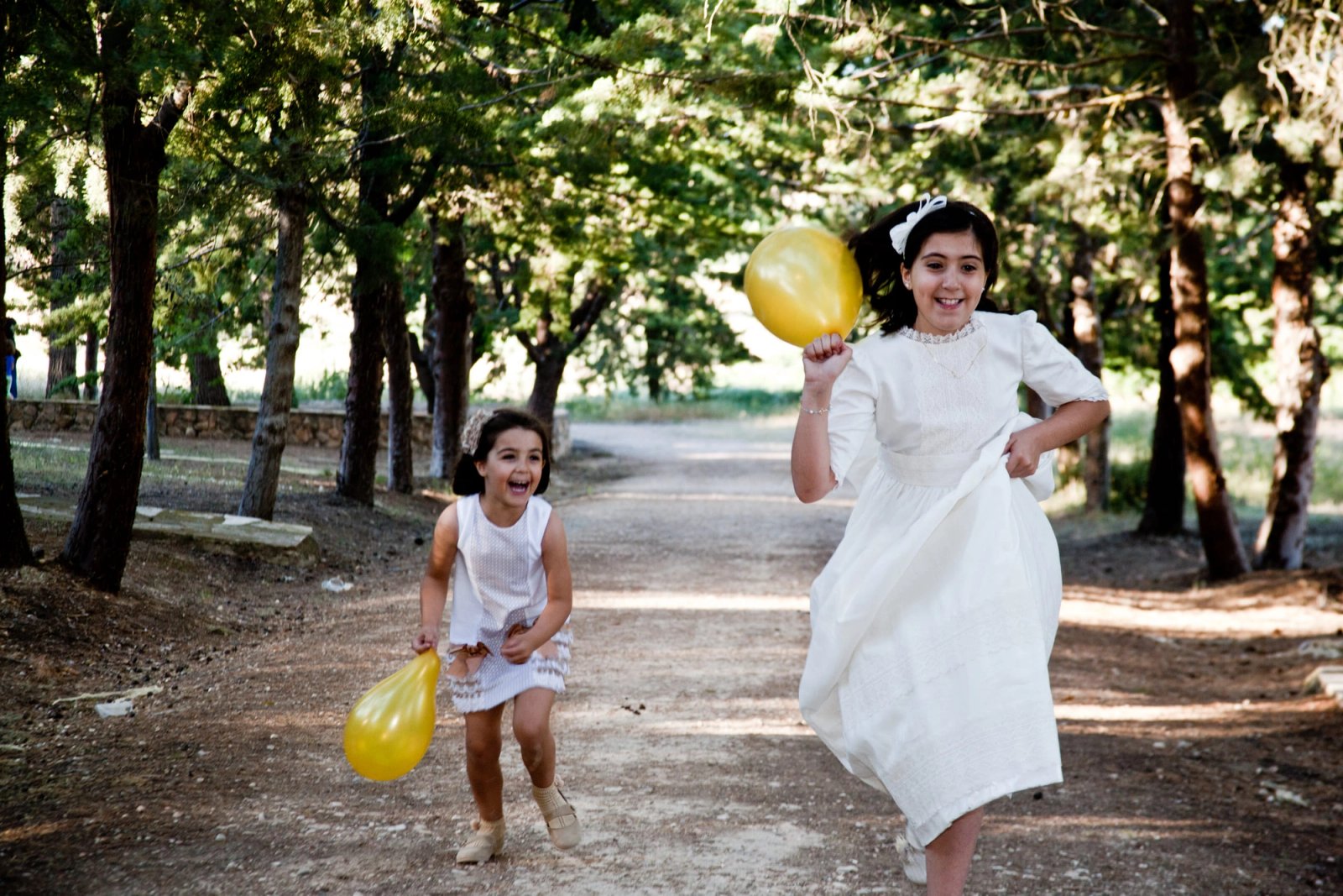 Dos niñas de comunión corren por un paseo con un globo