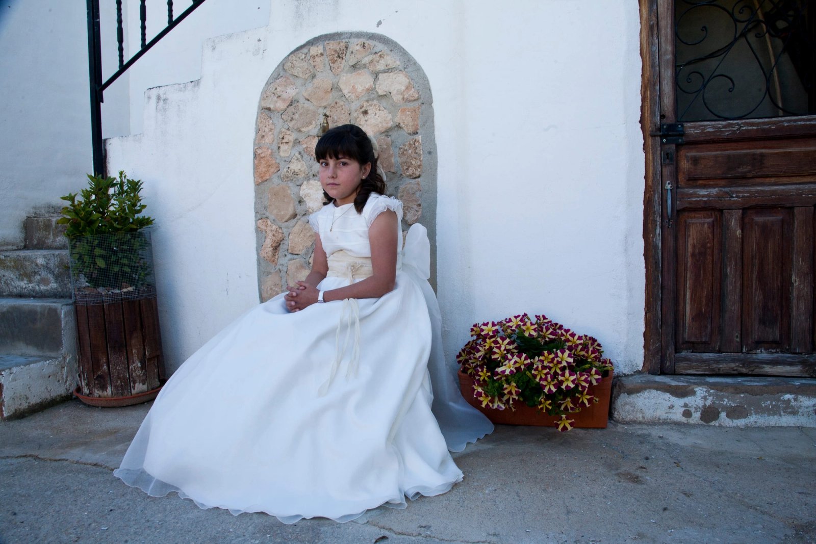 Una niña de comunión sentada junto a un portón antiguo