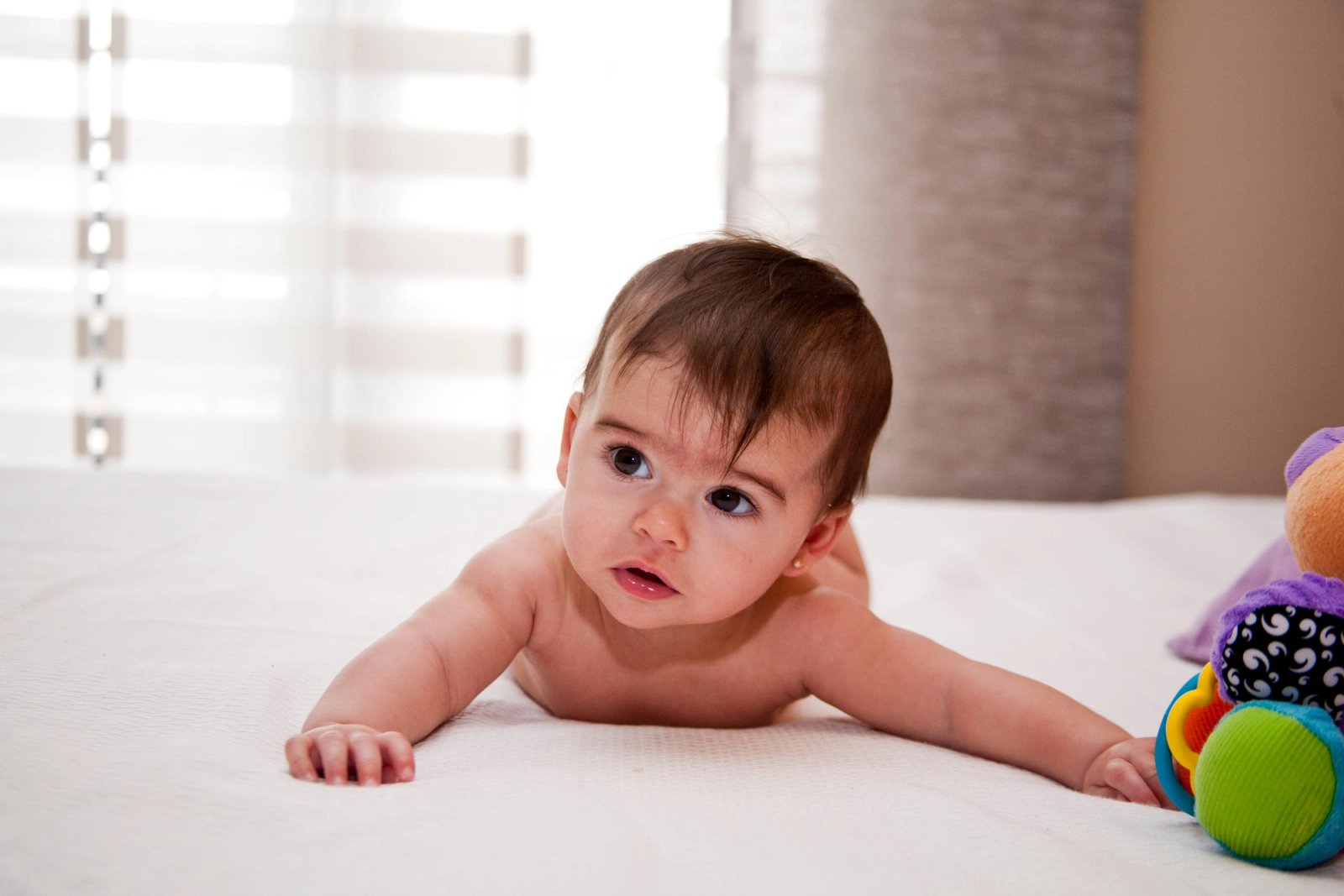 Un bebé boca abajo sobre la cama, mirando a cámara