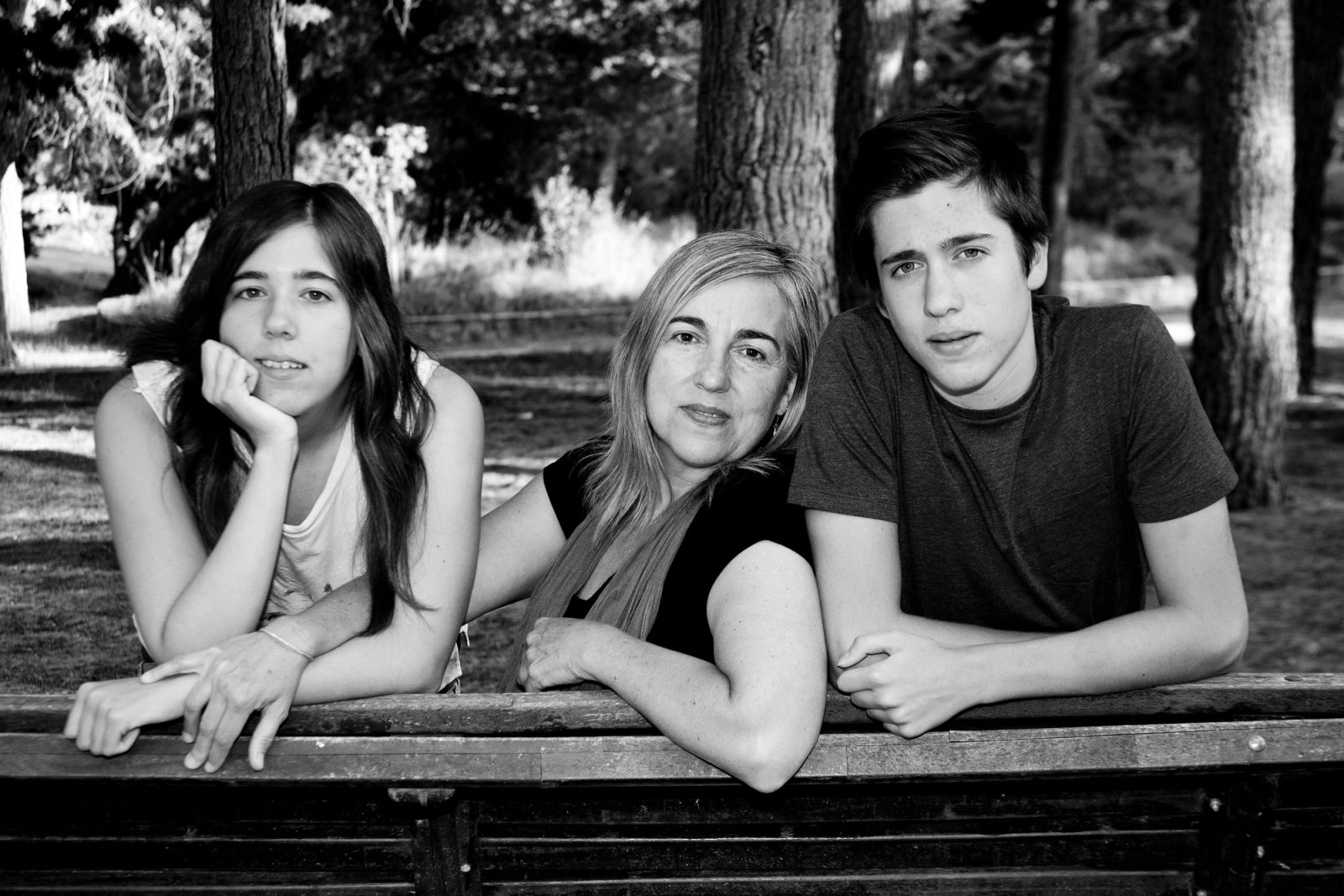 Una madre y sus hijos apoyados en un banco del parque, en blanco y negro