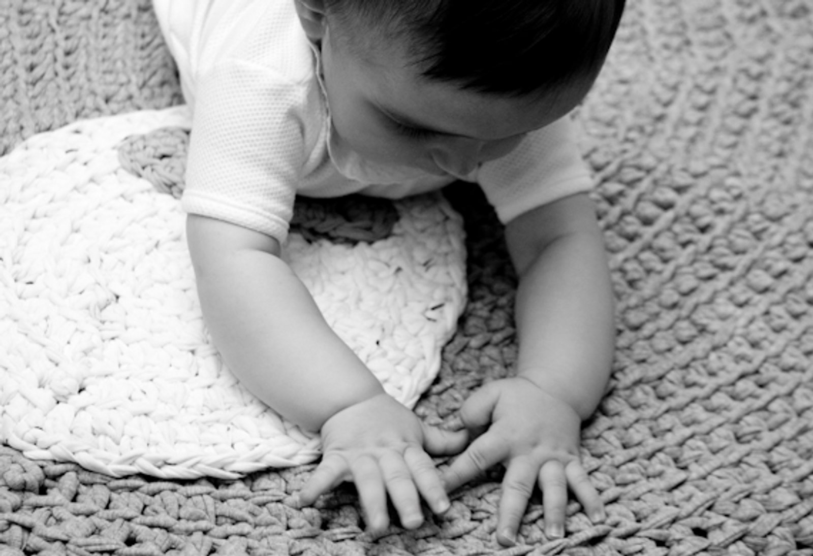 Las manos de un bebé sobre una manta de lana, en blanco y negro