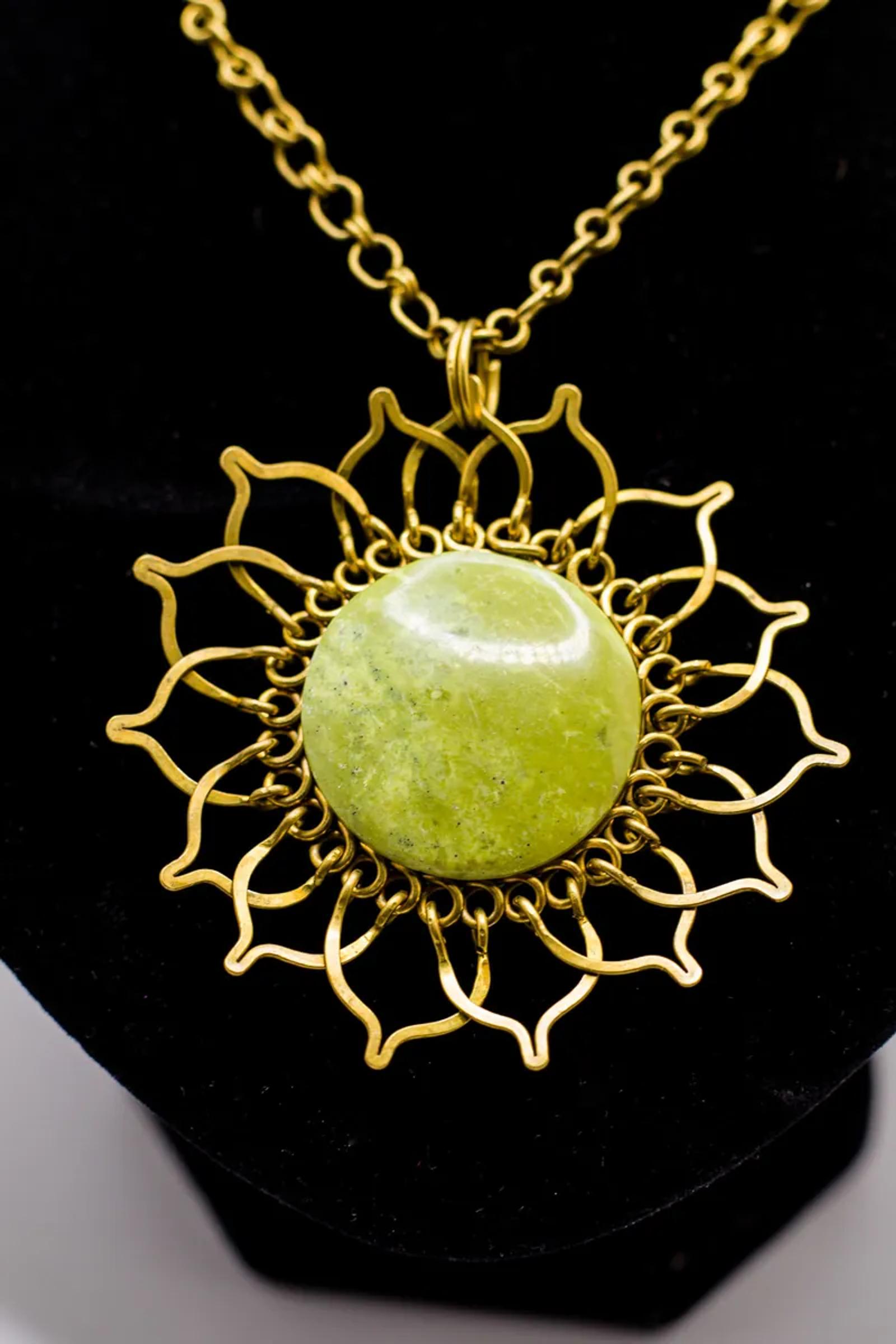 Gold pendant with a green stone on a display bust