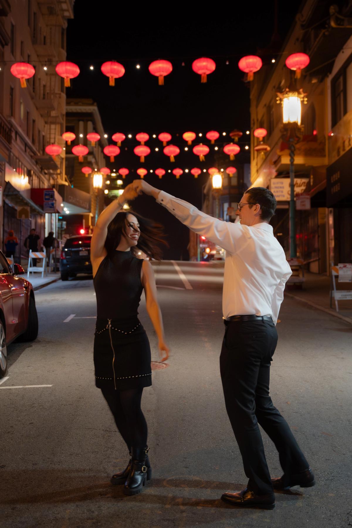 Couple dancing and spinning in the street at night beneath red lanterns in San Francisco's Chinatown, engagement session