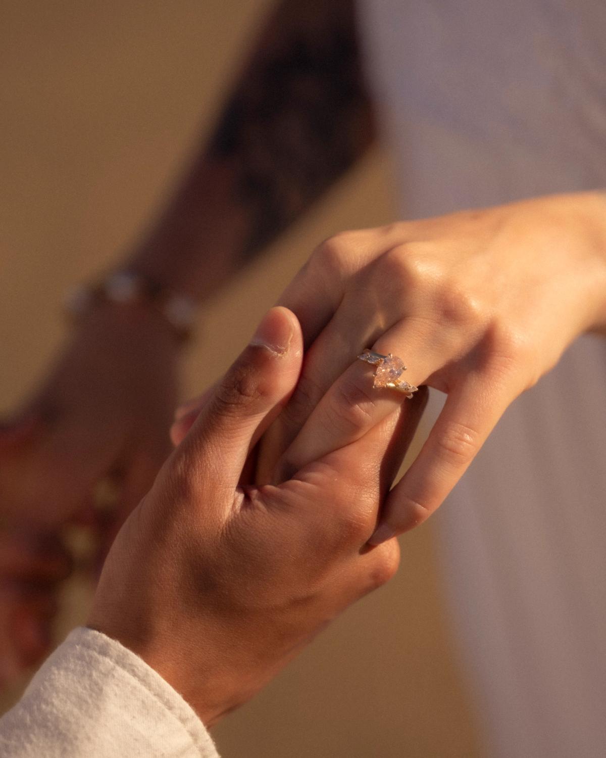 Detail shot of engagement ring on woman's hand held by partner, pear-cut diamond ring in warm natural light