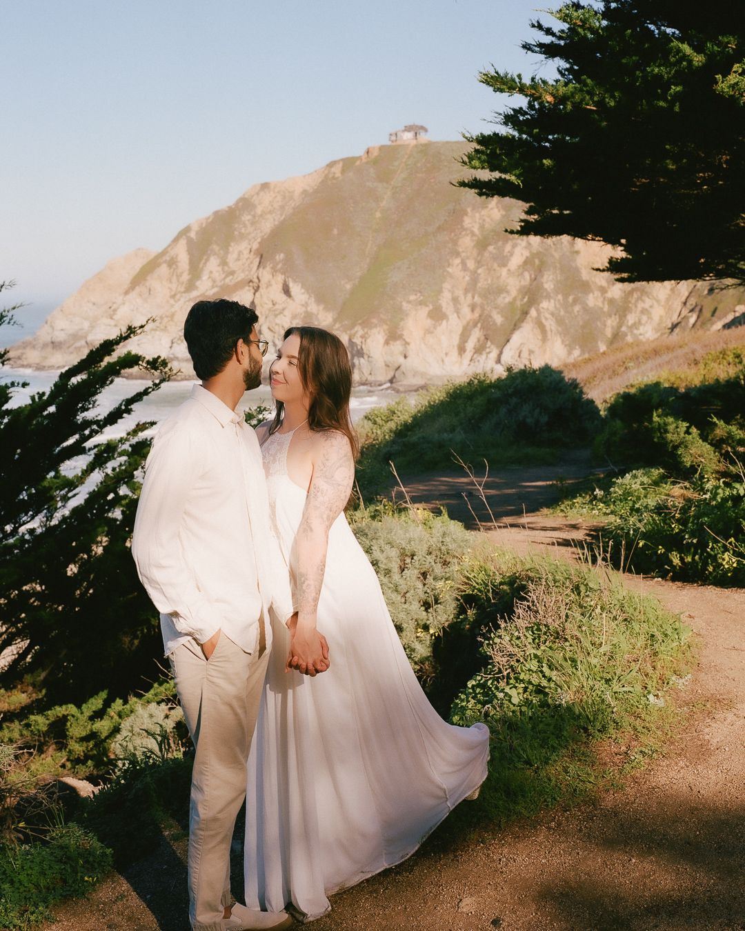 Engaged couple looking at each other under a tree on the California coast